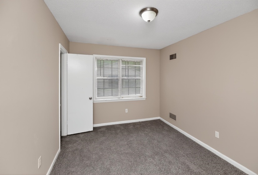 Carpeted room featuring neutral wall tones, white trim, and a double-hung window with grilles