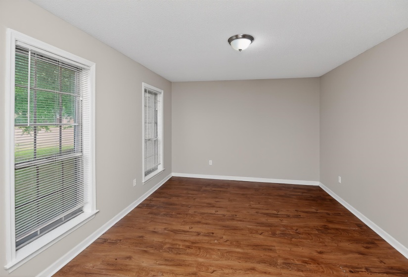 Spacious room featuring rich wood-finish flooring, light neutral wall tones, white trim, and two windows with blinds