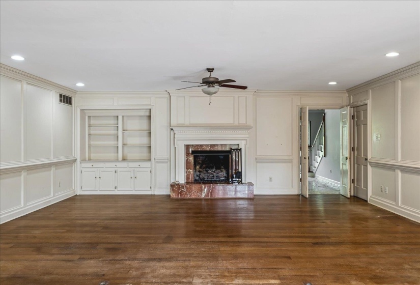 Spacious living area featuring rich wood-finish flooring, a decorative fireplace with a stone surround and hearth, and built-in shelving with lower cabinetry