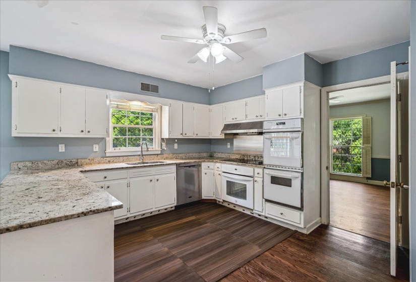 Kitchen featuring white cabinetry, light-toned countertops, integrated double ovens, a built-in dishwasher, and wood-finish flooring