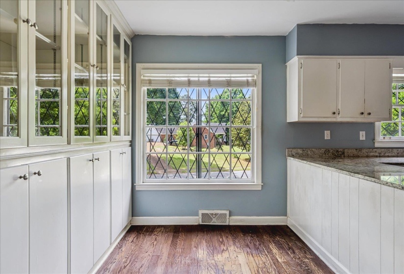 Wood-finish flooring complemented by a window with decorative muntins, built-in cabinetry featuring glass-front uppers, and a peninsula with a stone-finish countertop