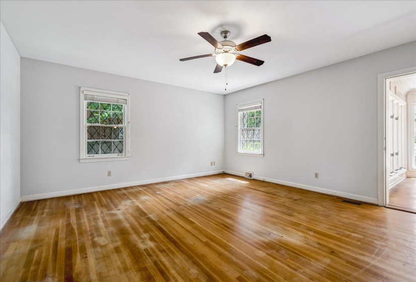 Spacious room featuring hardwood flooring, multiple windows, a ceiling fan with integrated lighting, and an open doorway leading to an additional space