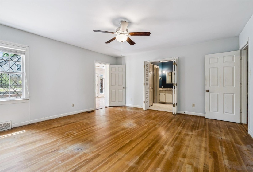Spacious room featuring wood-finish flooring, a ceiling fan with integrated lighting, and a window with decorative muntins