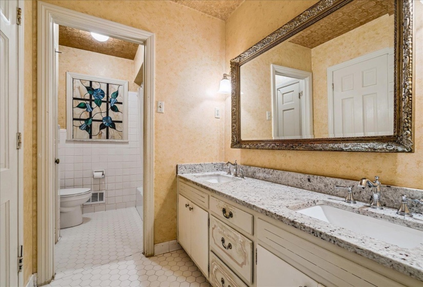Dual vanity with stone countertop and integrated sinks, ornate framed mirror, and decorative wall sconces