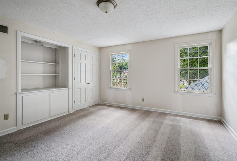 Carpeted room featuring two lattice-grid windows, built-in shelving, lower cabinetry, and bifold closet doors
