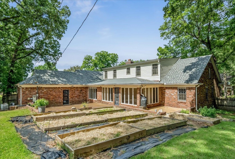 Rear exterior featuring a brick facade, white siding, multiple windows, and a covered patio area
