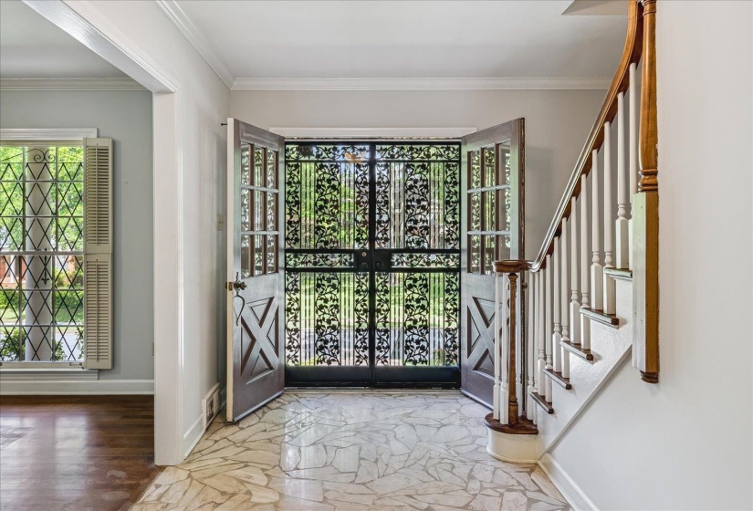 Entry foyer featuring a patterned tile floor, ornate iron double doors, and a hardwood staircase with white spindles