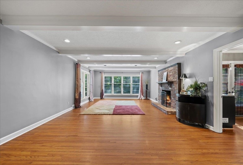 living room with beam ceiling, wood finished floors, with a brick fireplace