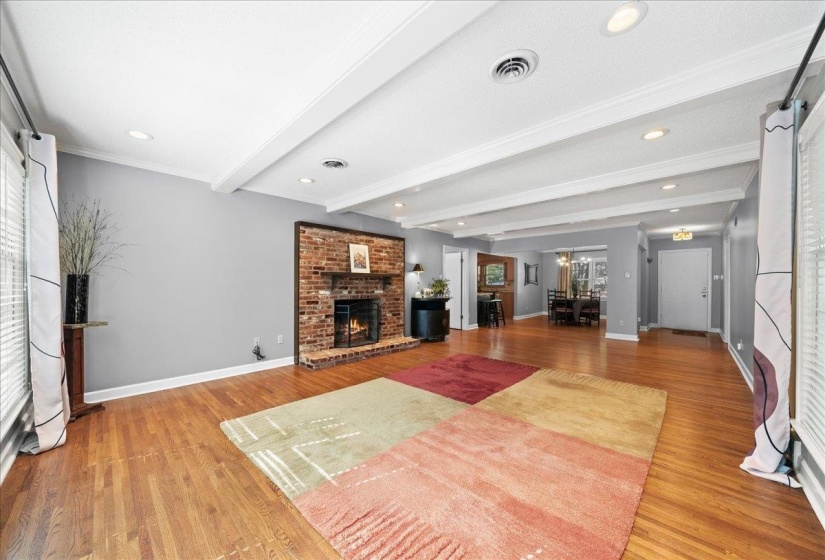 Living room with beam ceiling, a brick fireplace, light wood finished floors, and recessed lighting