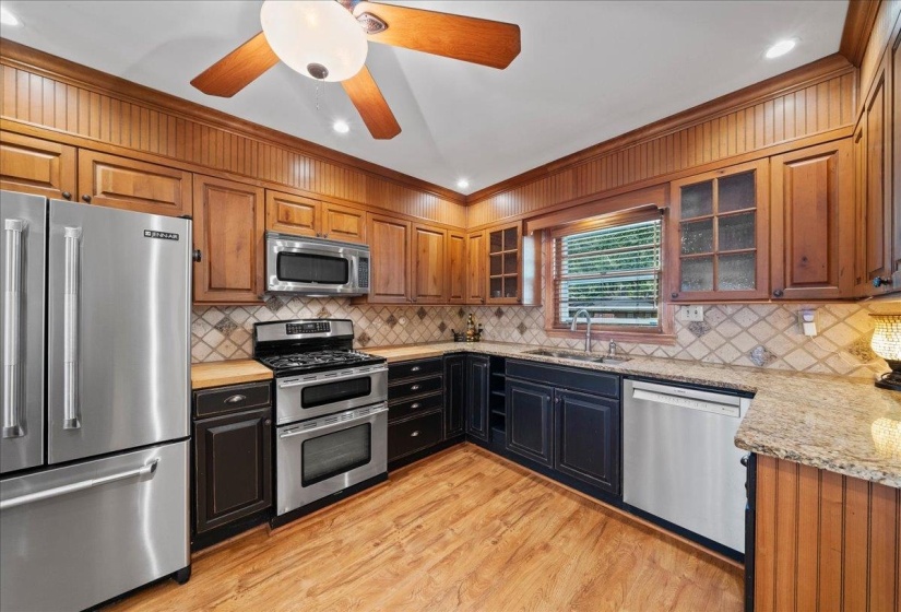 Kitchen featuring appliances with stainless steel finishes, glass insert cabinets, light granite counters, crown molding, and light wood-type flooring