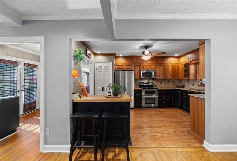Kitchen with appliances with stainless steel finishes, crown molding, light wood finished floors, glass insert cabinets, and brown cabinets and granite counters
