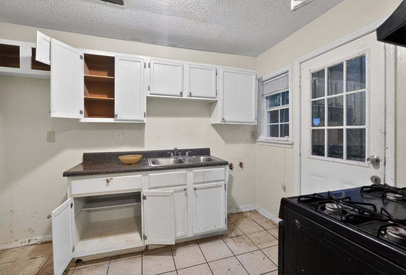 Kitchen featuring white cabinetry, a dark countertop, a double basin stainless steel sink, a gas range, and tiled flooring