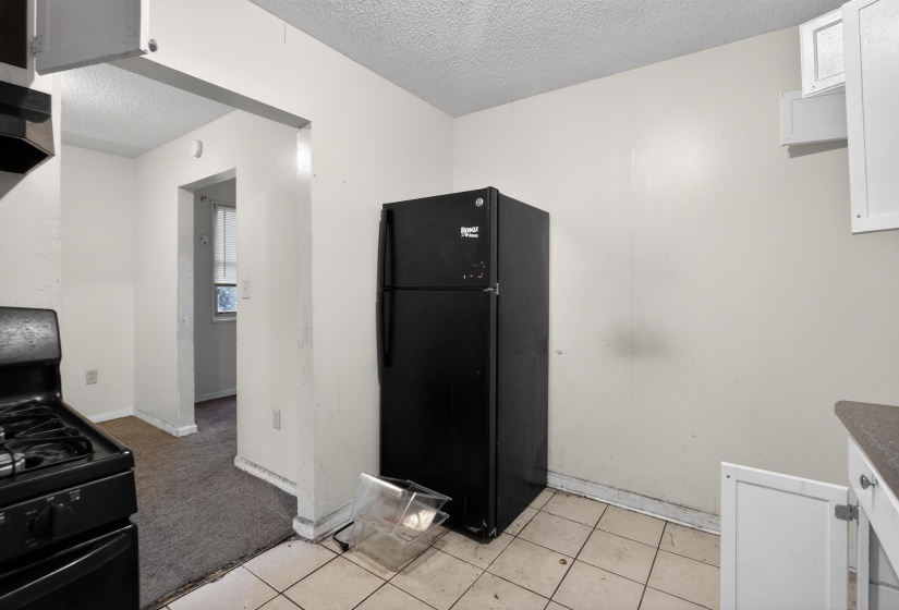 Kitchen area featuring a black refrigerator and range, upper and lower white cabinetry, and light-toned tile flooring