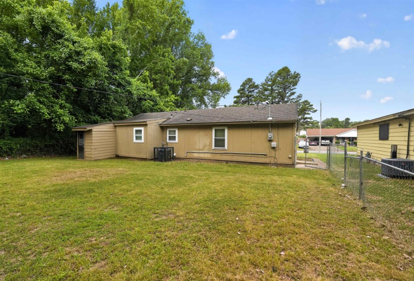 Expansive grassy backyard featuring a chain-link fence, mature trees, and a detached shed