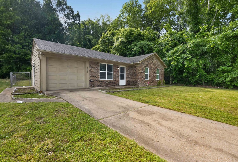 Brick facade home featuring an attached garage, a concrete driveway, and a chain-link fence