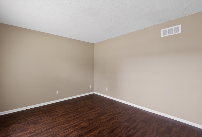 Interior space featuring wood-finish flooring, neutral wall paint, white trim, and a ceiling-mounted HVAC vent