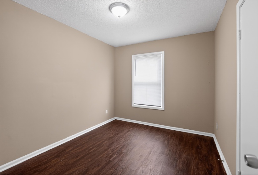 Room featuring wood-finish flooring, neutral wall paint, white trim, a single window, and a flush-mount ceiling light fixture