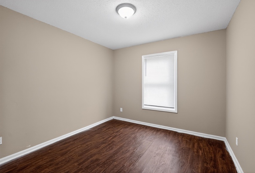 Room featuring wood-finish flooring, neutral wall tones, white baseboards, and a window with blinds
