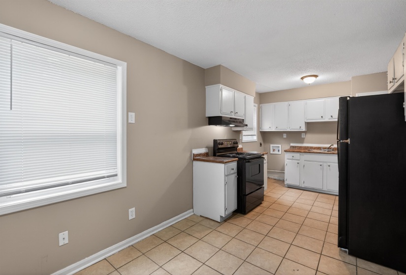 Kitchen featuring white cabinetry, wood-finish countertops, black appliances, and neutral tile flooring
