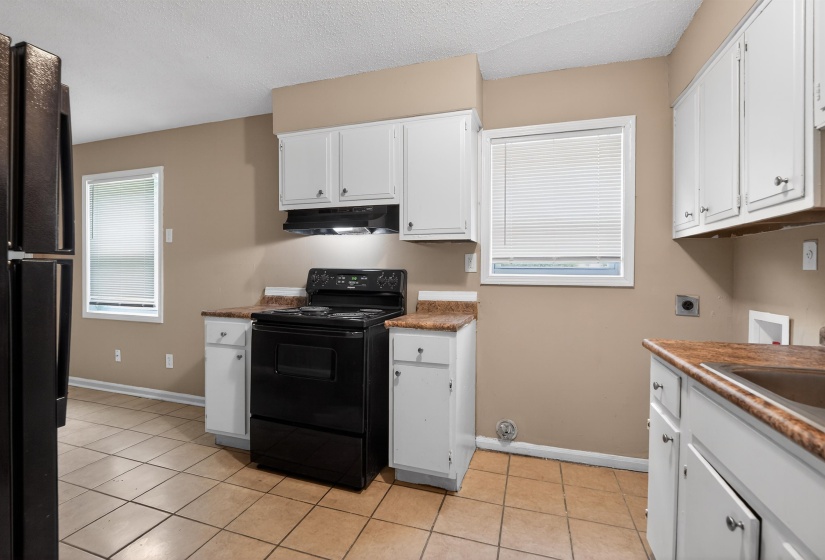 Kitchen area featuring white cabinetry, a black electric range with an overhead vent, and tile flooring