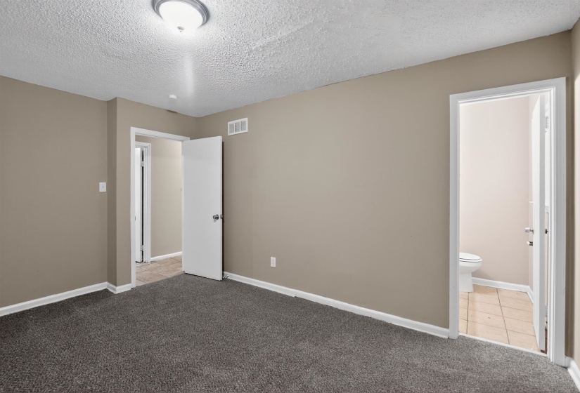 Neutral-toned interior room featuring dark gray carpet flooring, white baseboards, and a flush mount ceiling light fixture