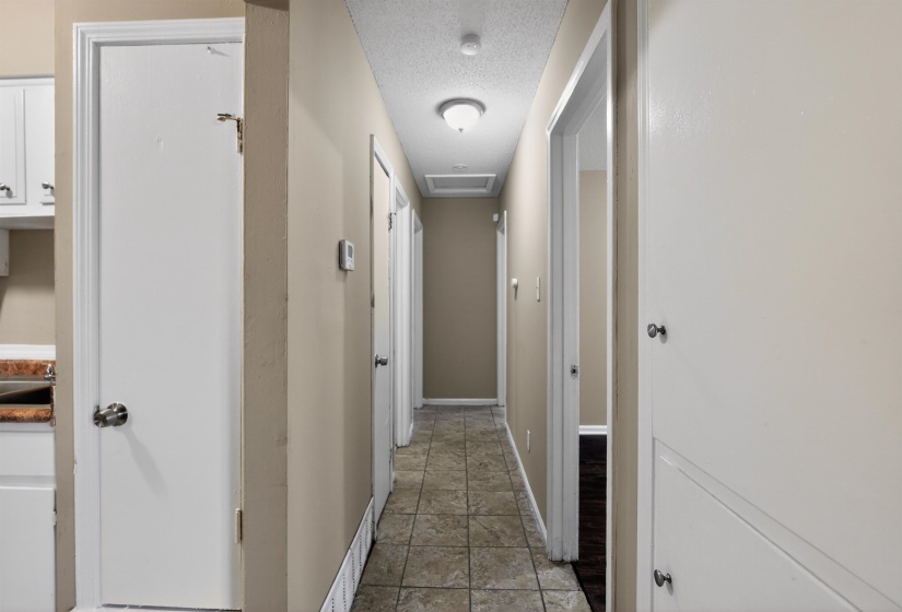 Hallway with neutral wall paint, ceiling-mounted lighting, and square tile flooring