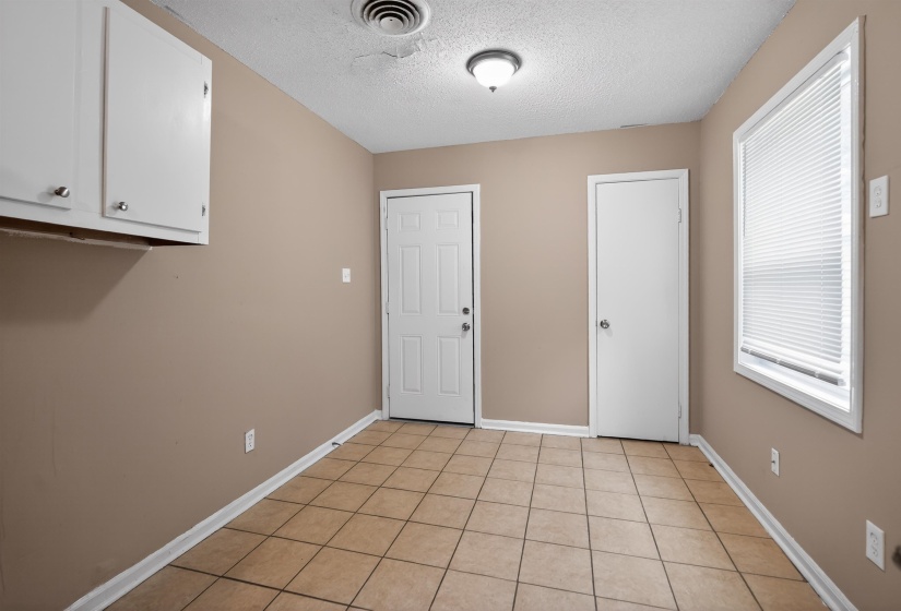 Tile flooring, neutral wall paint, two white doors, white window blinds, and white upper cabinetry