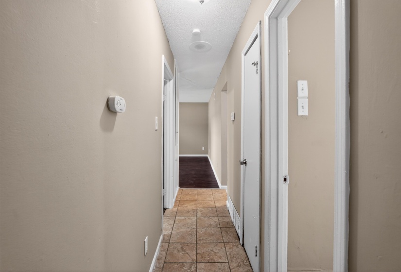 Hallway featuring neutral wall tones, square tile flooring, white trim, and doors with silver hardware