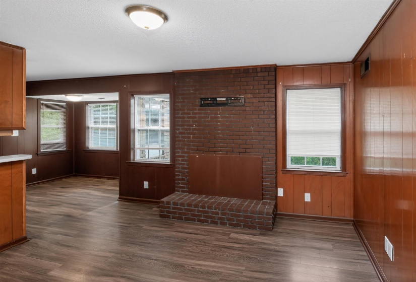 Brick fireplace with hearth, wood-finish flooring, multiple windows with blinds, and paneled walls