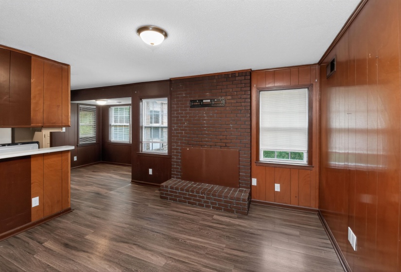 Spacious room featuring wood-finish flooring, a brick fireplace with hearth, wood paneling, and multiple windows