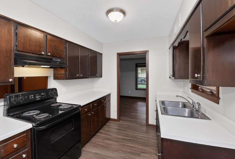 Kitchen featuring wood-finish flooring, dark wood cabinetry, white countertops, and a black electric range