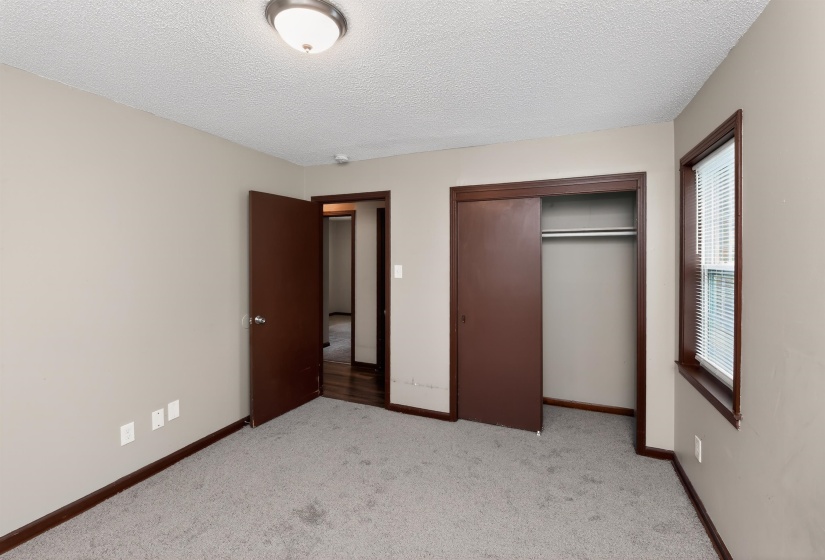 Neutral-toned room featuring a single window with blinds, a built-in closet with sliding doors, and a ceiling-mounted light fixture