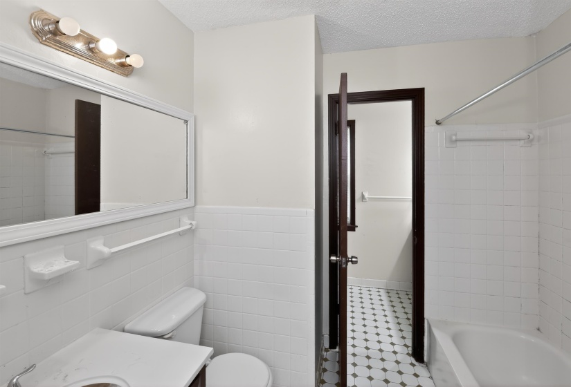 Bathroom featuring a white subway tile wainscoting, a white tub with tile surround, a vanity with an integrated sink, and a rectangular mirror with overhead lighting