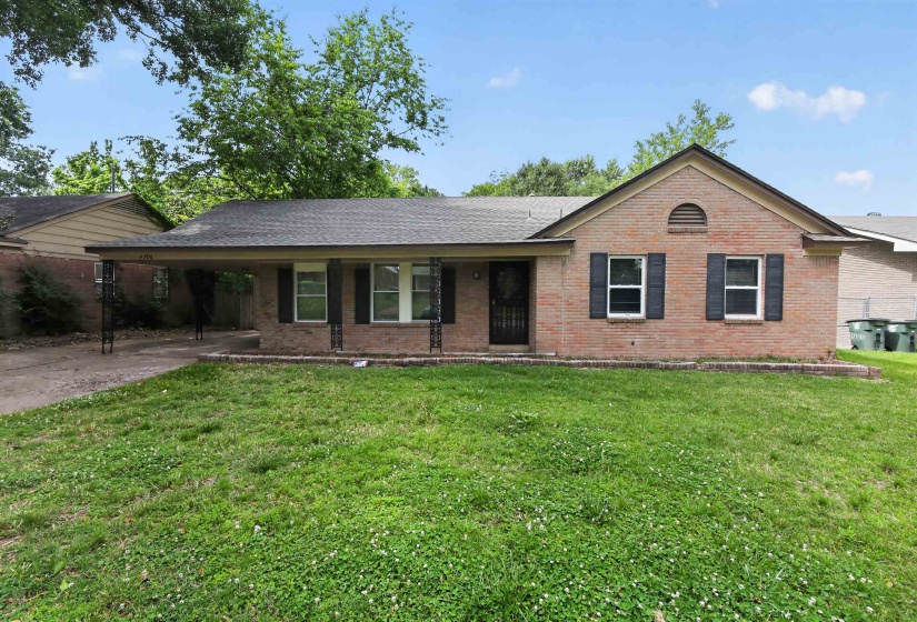 Brick exterior home featuring a covered entryway, attached carport, black shutters, and an arched vent detail