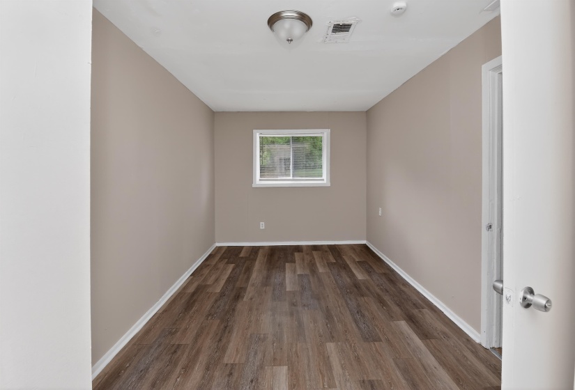 Neutral-toned room featuring wood-finish flooring, white baseboards, and a single window with white trim