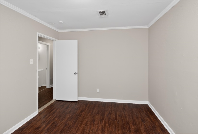 Room featuring wood-finish flooring, light neutral wall paint, white baseboards, and white crown molding