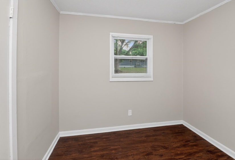 Neutral tone walls with white trim, wood-finish flooring, and a single window with blinds