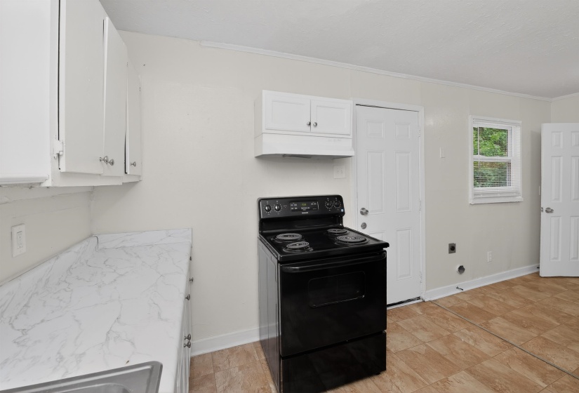 Kitchen featuring white cabinetry, a black electric range, a white countertop with a subtle veining pattern, a stainless steel sink, and wood-finish flooring