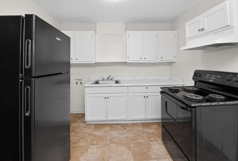 Kitchen featuring black appliances, white cabinetry, a stainless steel sink, and light-toned flooring