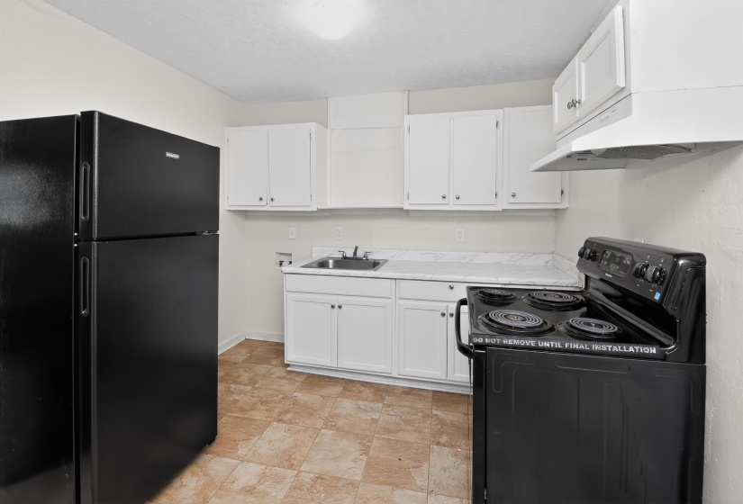 Kitchen featuring white cabinetry, a black electric range with an overhead vent, a black refrigerator, a stainless steel sink, and patterned flooring