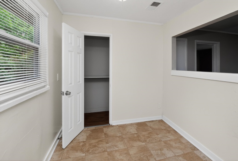 Room featuring tiled flooring, a window with blinds, a closet with an open six-panel door, and a wall cutout