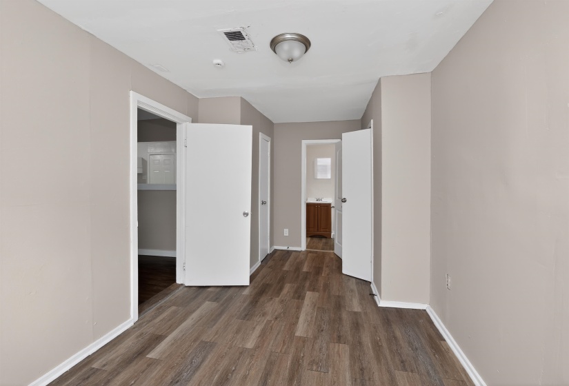 Interior corridor featuring wood-finish flooring, light neutral wall paint, white baseboards, and white interior doors