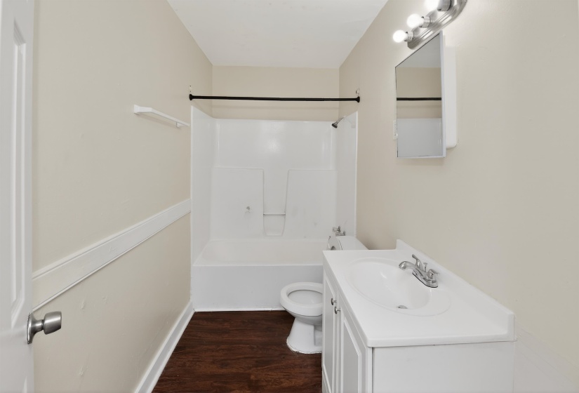 Bathroom featuring a white vanity with integrated sink, white bathtub and shower surround, dark wood-finish flooring, and neutral painted walls