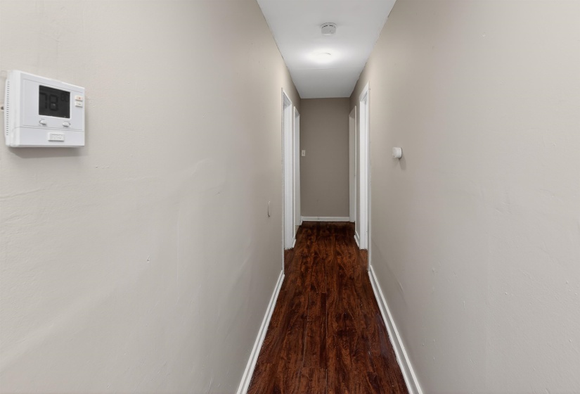 Hallway featuring wood-finish flooring, light neutral wall paint, and white baseboards