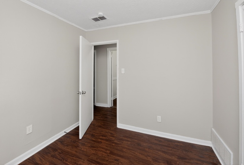 Interior room featuring neutral wall paint, wood-finish flooring, white baseboards, and crown molding