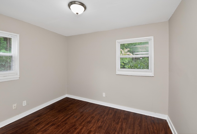 Room featuring wood-finish flooring, neutral wall paint, white trim, two windows with blinds, and a ceiling-mounted light fixture