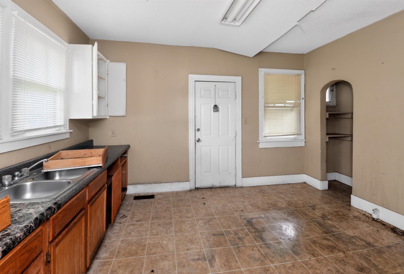 Kitchen space with tiled flooring, a double basin stainless steel sink, wood cabinetry, and white upper cabinets