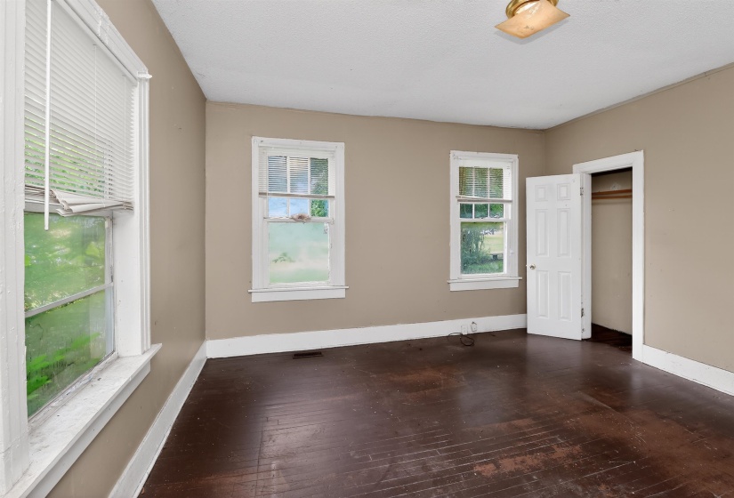 Spacious room featuring dark wood-finish flooring, light tan wall color, and white trim