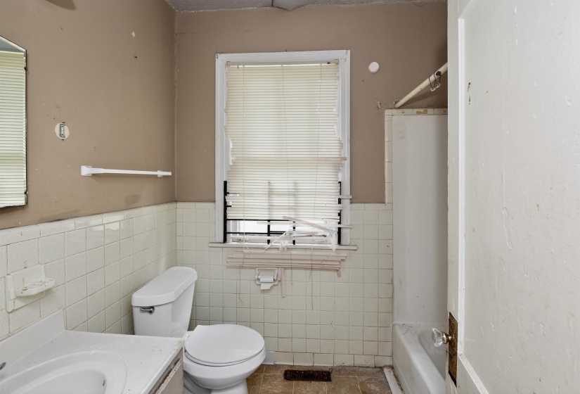Bathroom featuring a window with blinds, white wall tiling, a toilet, a sink vanity, and a bathtub