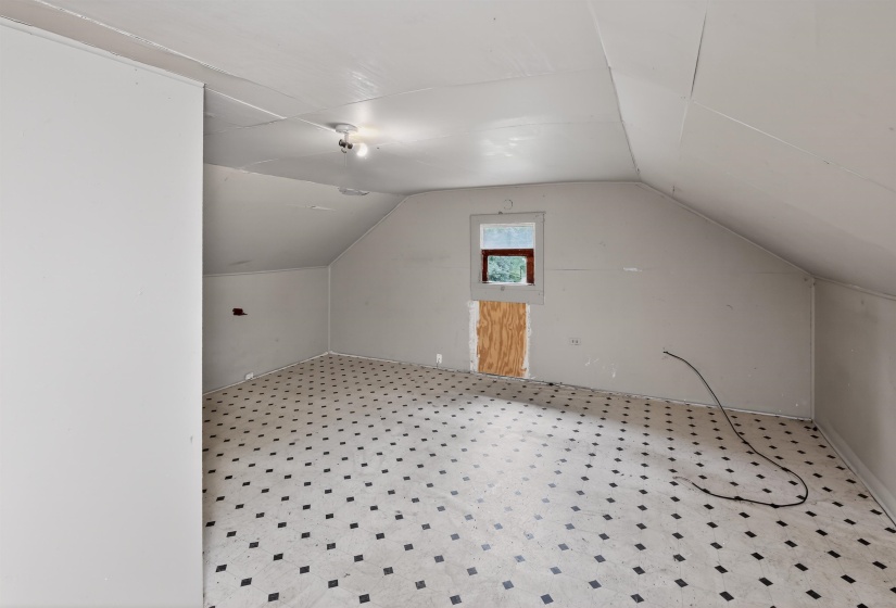 Spacious room featuring patterned flooring, sloped ceilings, and a framed window opening